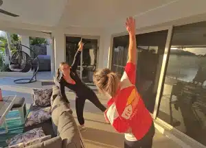 Fit Your Ability trainer guiding a client through a standing side stretch with a dumbbell on a home patio