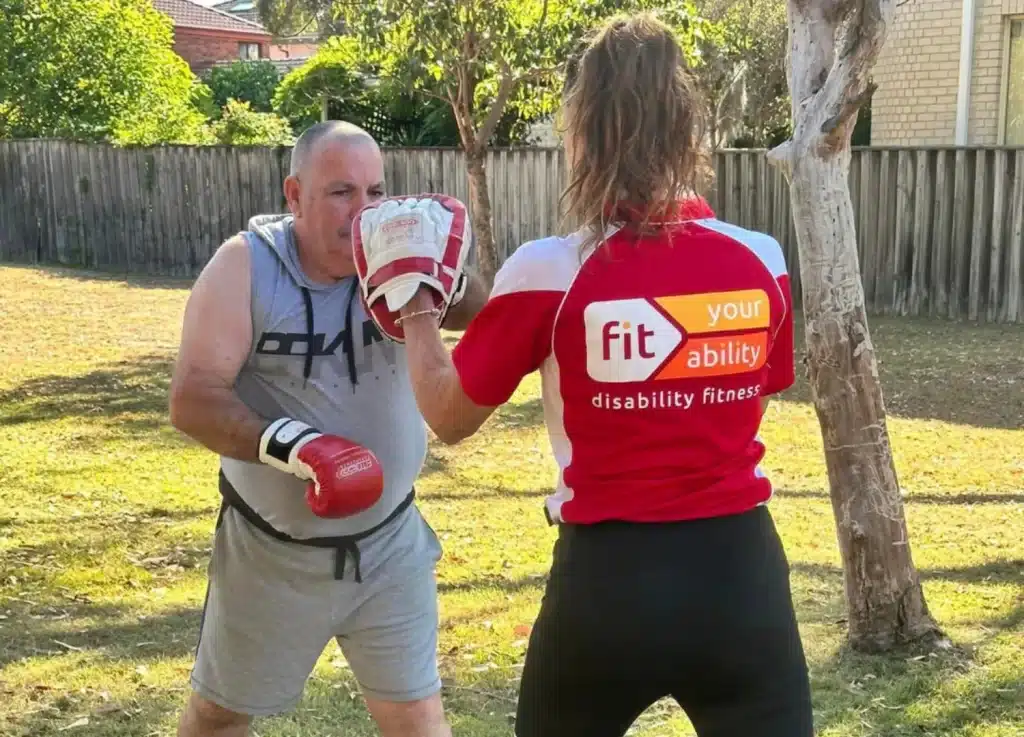 Fit Your Ability disability fitness trainer holding focus pads for a client wearing boxing gloves in a backyard